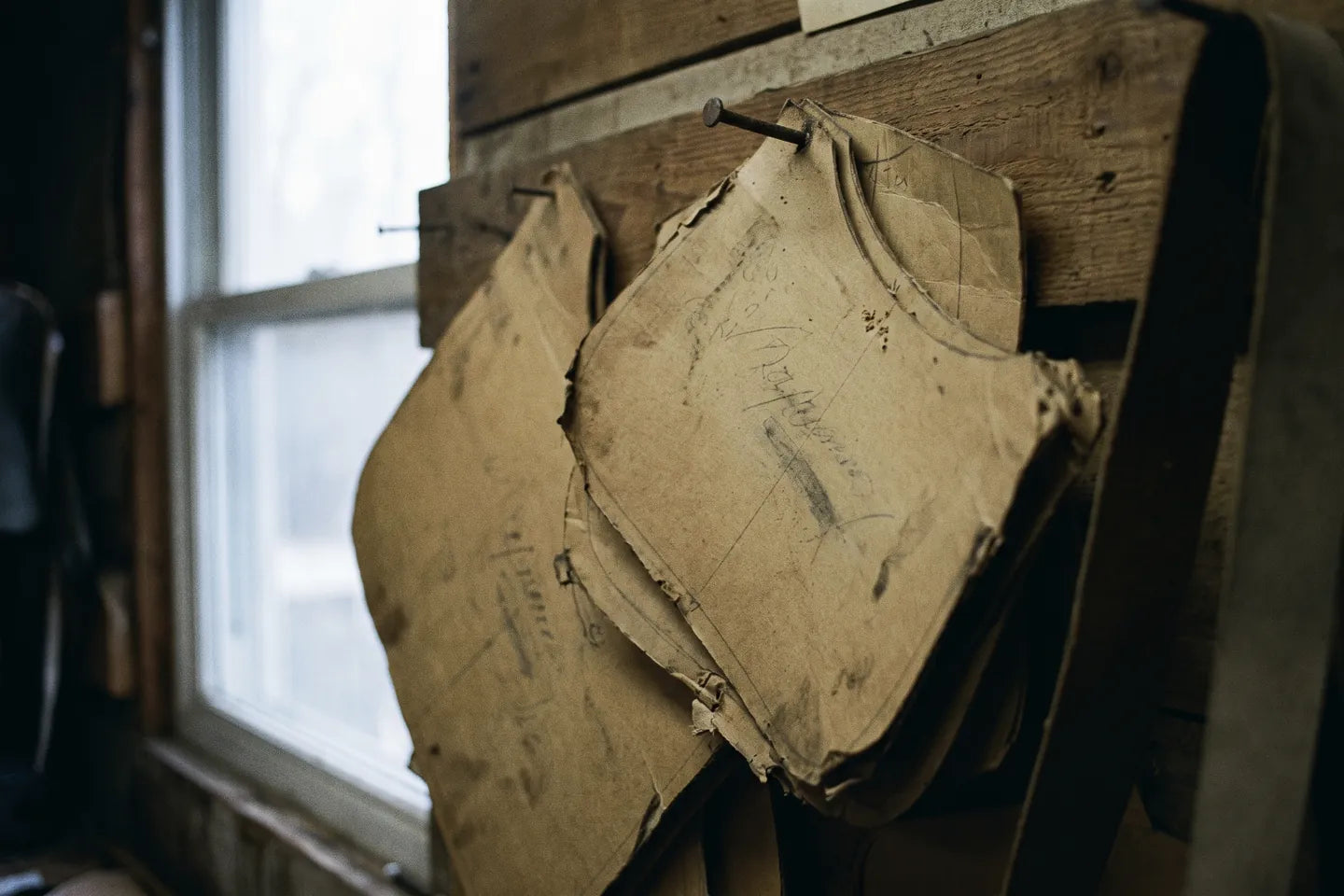 Worn manila pattern pieces hanging on a nail, the pencil initials rubbed away.