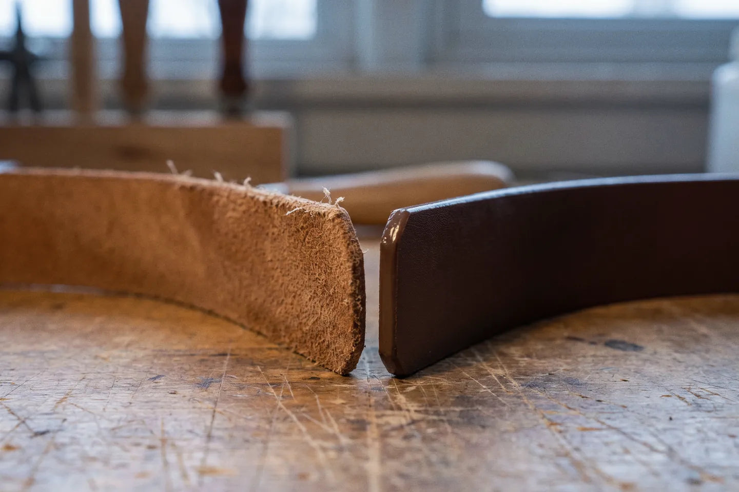 Two cut strap edges side by side in window light: fibrous real leather, and sealed coated material.